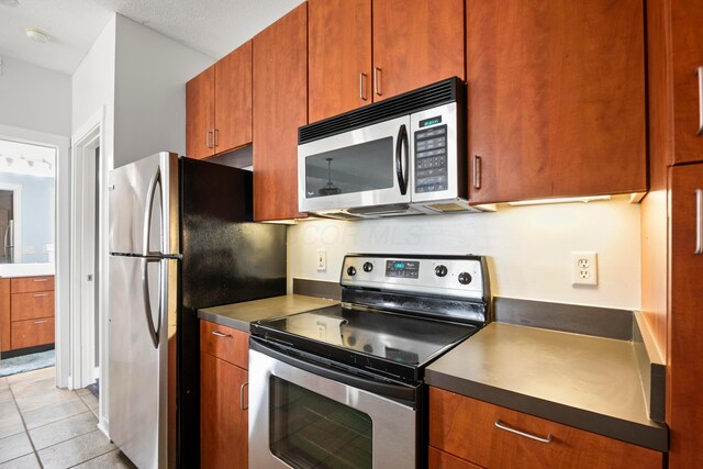 kitchen with stainless steel appliances, brown cabinetry, and light tile patterned floors