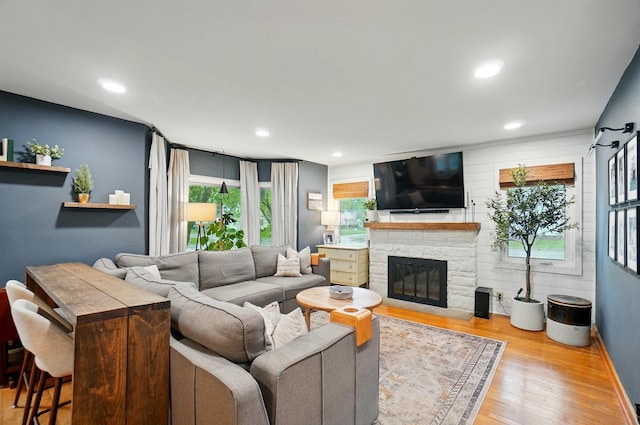 living room with wood finished floors, a stone fireplace, recessed lighting, and baseboards