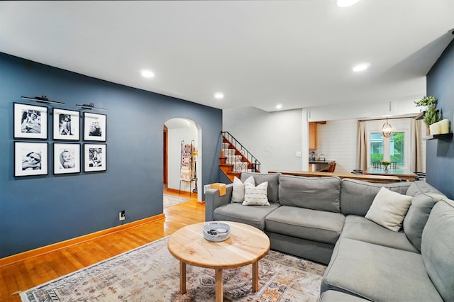living room featuring arched walkways, light wood finished floors, recessed lighting, stairway, and baseboards