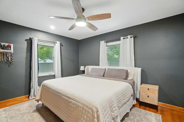bedroom with multiple windows, wood finished floors, baseboards, and a ceiling fan