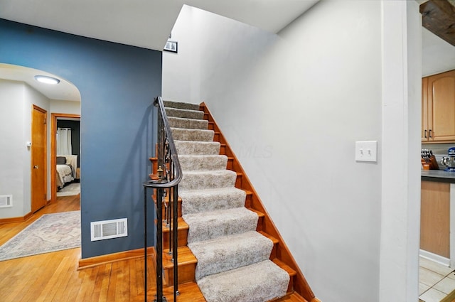 staircase featuring arched walkways, wood finished floors, and baseboards