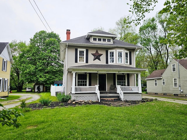 american foursquare style home with covered porch, a chimney, and a front lawn