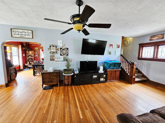 living room with wood finished floors, arched walkways, a textured ceiling, ceiling fan, and healthy amount of natural light