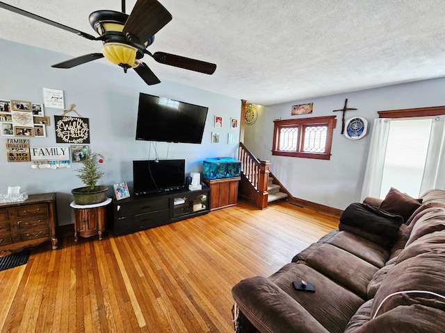 living area featuring a textured ceiling, wood finished floors, a ceiling fan, stairway, and baseboards