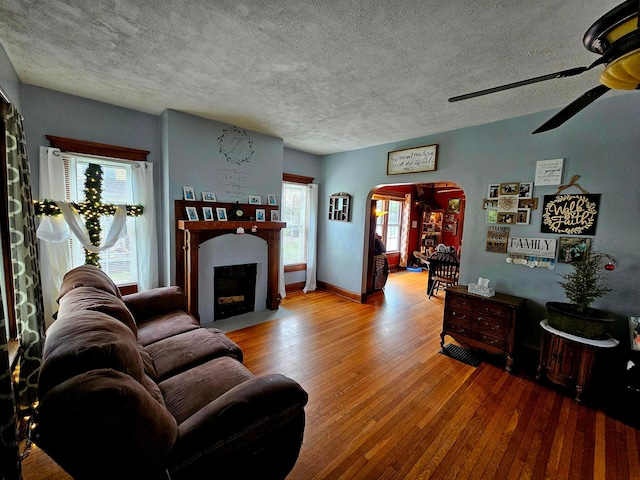 living room featuring arched walkways, hardwood / wood-style flooring, ceiling fan, a textured ceiling, and a fireplace with flush hearth