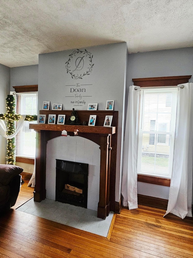 detailed view of wood finished floors, a textured ceiling, a tiled fireplace, and baseboards