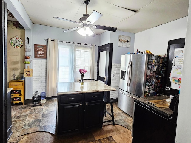 kitchen with electric range, dark cabinets, a ceiling fan, stainless steel fridge with ice dispenser, and dark stone finish floors