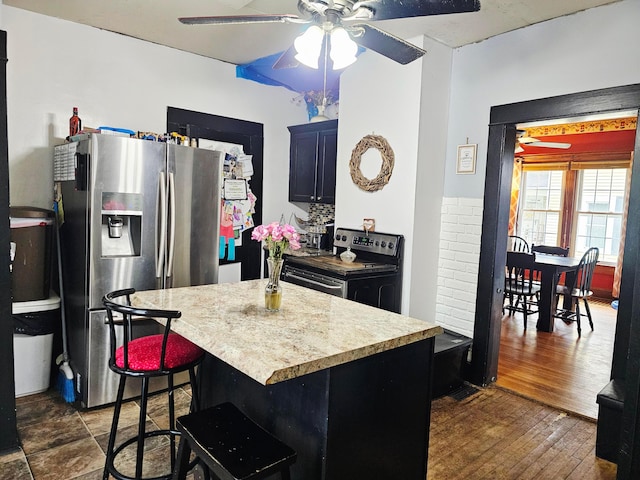 kitchen featuring appliances with stainless steel finishes, a ceiling fan, light countertops, a kitchen island, and a breakfast bar