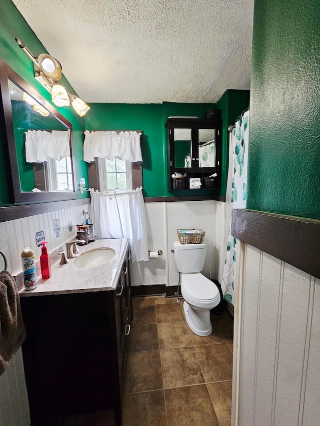bathroom featuring a textured ceiling, vanity, a wainscoted wall, and toilet