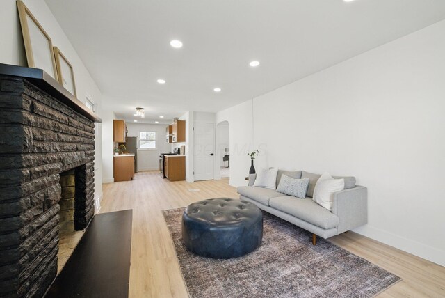 living area with arched walkways, light wood-style flooring, recessed lighting, a brick fireplace, and baseboards