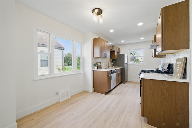 kitchen with stainless steel appliances, under cabinet range hood, tasteful backsplash, light wood-style flooring, and recessed lighting