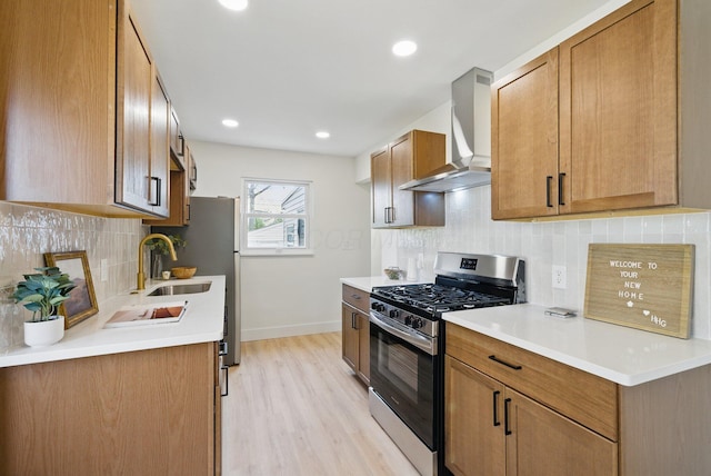 kitchen featuring gas stove, wall chimney range hood, a sink, baseboards, and light wood-style floors