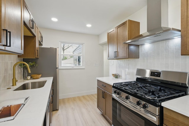 kitchen featuring wall chimney exhaust hood, stainless steel gas range, a sink, light wood finished floors, and backsplash