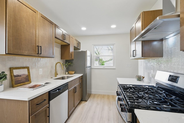kitchen with stainless steel appliances, wall chimney exhaust hood, a sink, light wood-style floors, and light countertops