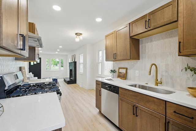 kitchen with stainless steel appliances, a sink, exhaust hood, a brick fireplace, and decorative backsplash