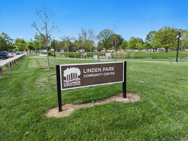 community / neighborhood sign featuring a lawn and a water view
