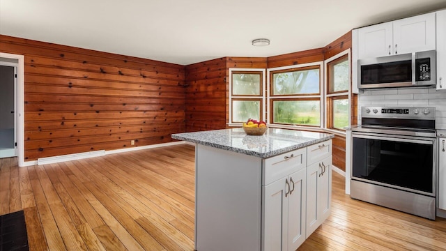 255 S Preston St, Centerburg, OH 43011 - kitchen with stainless steel appliances, light wood-style floors, white cabinets, a center island, and wooden walls
