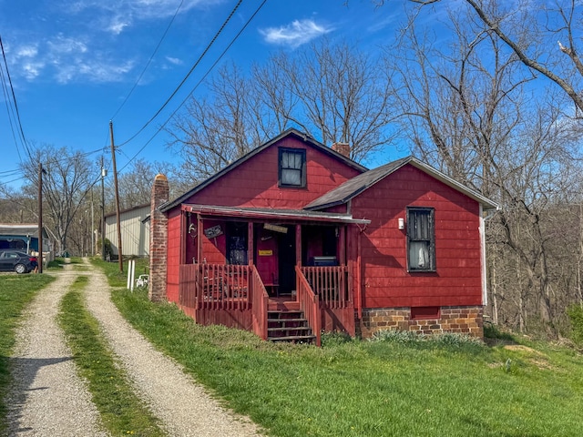 view of front of home with a chimney, covered porch, driveway, a front yard, and roof with shingles