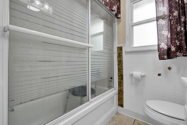 bathroom featuring tile patterned floors, toilet, bath / shower combo with glass door, and tile walls