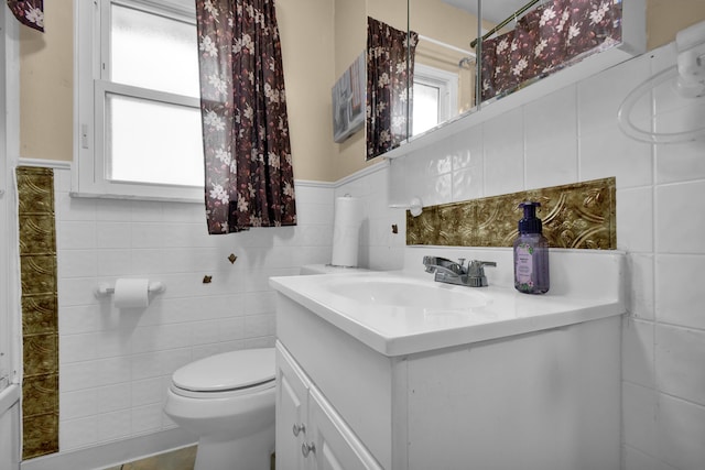 bathroom with tile walls, toilet, vanity, and a wainscoted wall