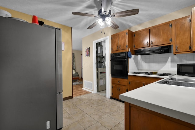 kitchen with black appliances, under cabinet range hood, brown cabinets, a ceiling fan, and decorative backsplash