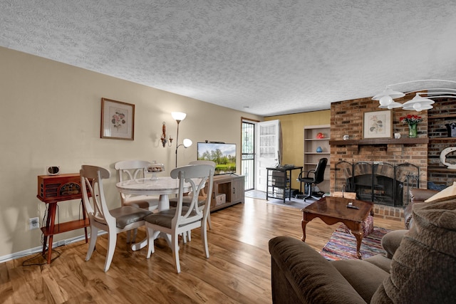 dining room with wood finished floors, baseboards, a textured ceiling, and a brick fireplace