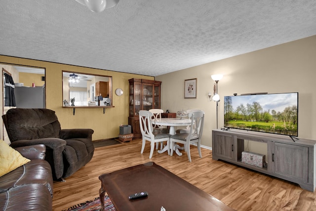 living area with a textured ceiling, wood finished floors, baseboards, and a ceiling fan