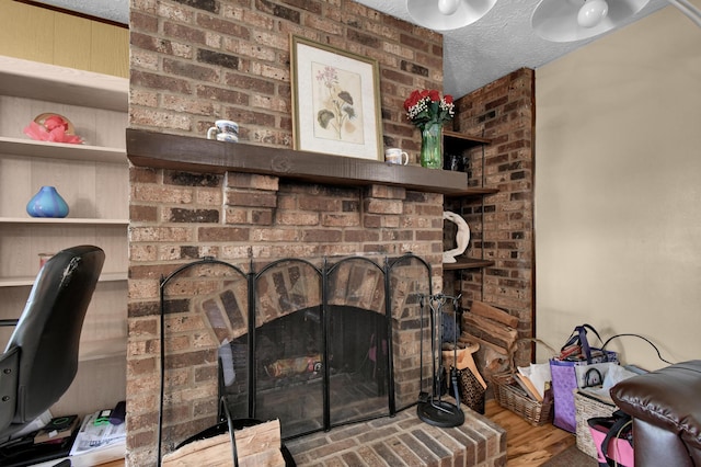 detailed view of a brick fireplace, wood finished floors, and a textured ceiling