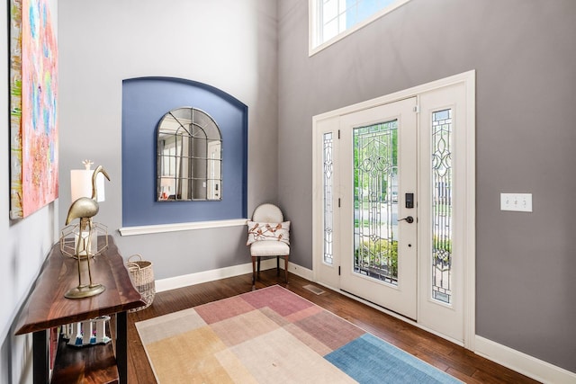 foyer entrance featuring wood finished floors, a towering ceiling, and baseboards