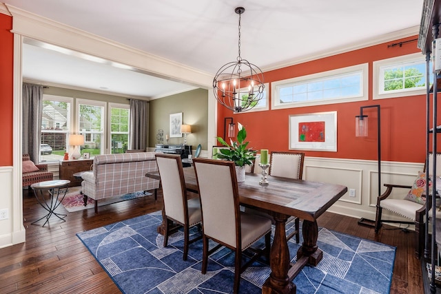 dining area with dark wood finished floors, a wainscoted wall, ornamental molding, a chandelier, and a decorative wall