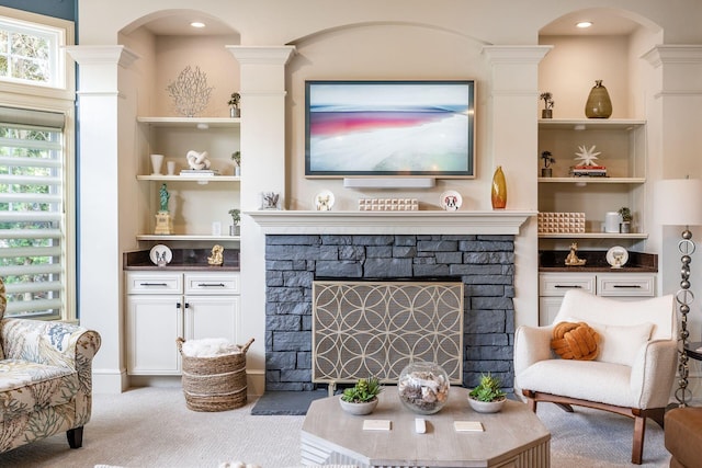 living area with arched walkways, a stone fireplace, carpet, ornate columns, and recessed lighting