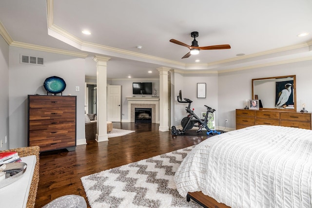 bedroom with ornate columns, a tray ceiling, wood finished floors, crown molding, and a fireplace