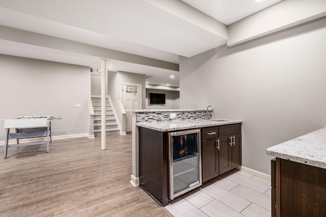 kitchen with beverage cooler, dark brown cabinetry, light wood-type flooring, light stone countertops, and recessed lighting