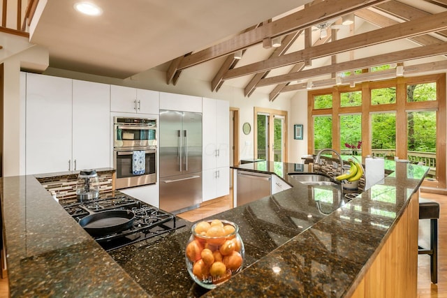 kitchen featuring stainless steel appliances, a sink, decorative backsplash, white cabinets, and a breakfast bar area