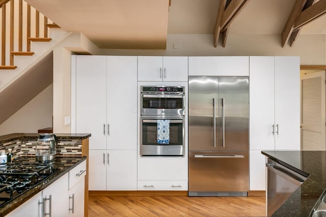 kitchen with appliances with stainless steel finishes, light wood-style floors, dark stone countertops, white cabinets, and decorative backsplash