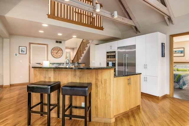 kitchen featuring appliances with stainless steel finishes, light wood-style floors, a breakfast bar, beam ceiling, and baseboards
