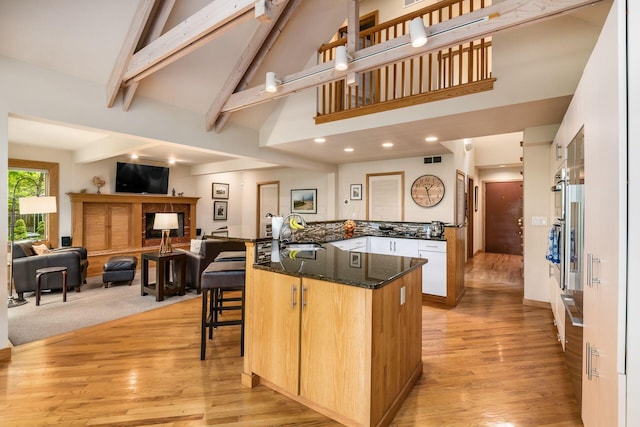 kitchen featuring high vaulted ceiling, a sink, light wood finished floors, a breakfast bar, and beamed ceiling