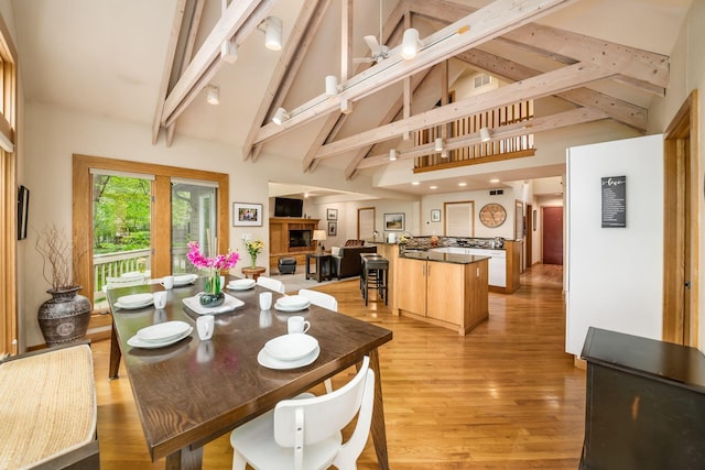 dining area featuring high vaulted ceiling, beam ceiling, light wood finished floors, and a fireplace