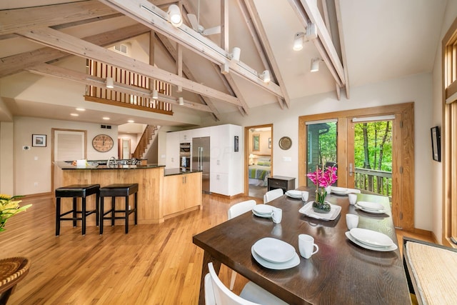 dining area featuring high vaulted ceiling, beam ceiling, light wood-type flooring, baseboards, and stairs