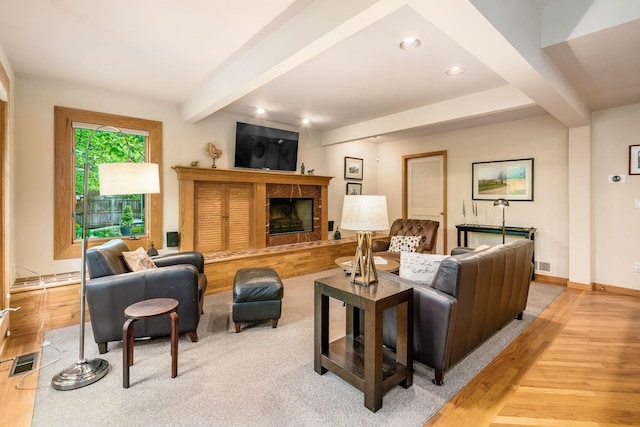 living area with beam ceiling, recessed lighting, light wood finished floors, a tiled fireplace, and baseboards
