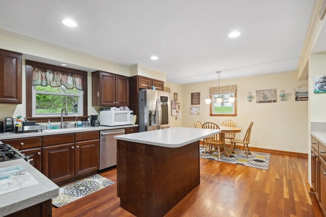 kitchen with stainless steel appliances, a sink, light countertops, wood finished floors, and a kitchen island