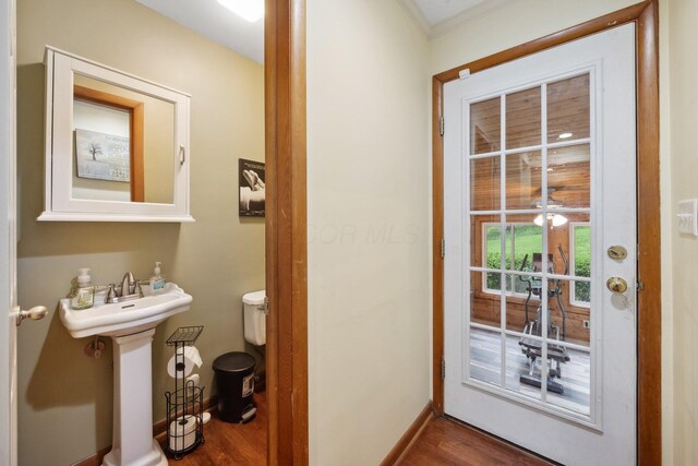 bathroom featuring wood finished floors, baseboards, crown molding, toilet, and a sink