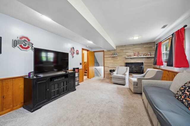 carpeted living area with wooden walls, a stone fireplace, and stairway