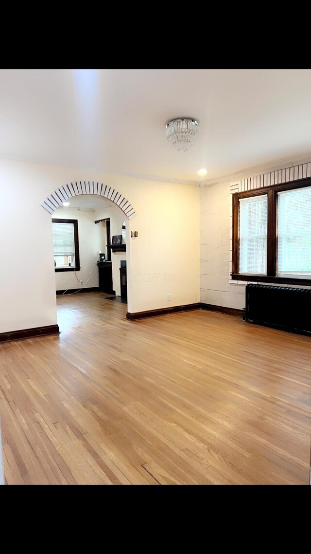 1065 Sunbury Rd, Columbus, OH 43219 - unfurnished living room featuring light wood-style flooring, arched walkways, and radiator