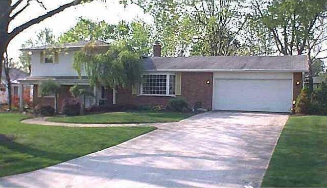 tri-level home with concrete driveway, an attached garage, a front yard, and a chimney
