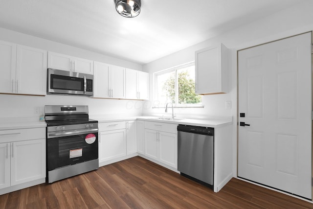 kitchen featuring appliances with stainless steel finishes, a sink, dark wood-type flooring, light countertops, and white cabinetry