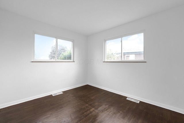 spare room with baseboards, plenty of natural light, and dark wood finished floors