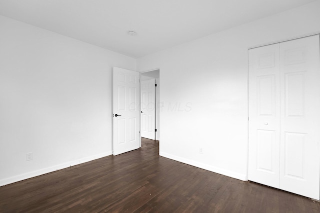 unfurnished bedroom with dark wood-style floors, baseboards, and a closet