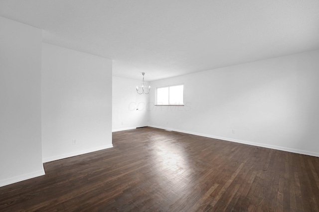 unfurnished room with a chandelier, dark wood-type flooring, and baseboards