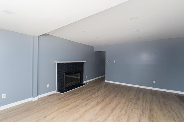 unfurnished living room featuring wood finished floors, baseboards, and a brick fireplace
